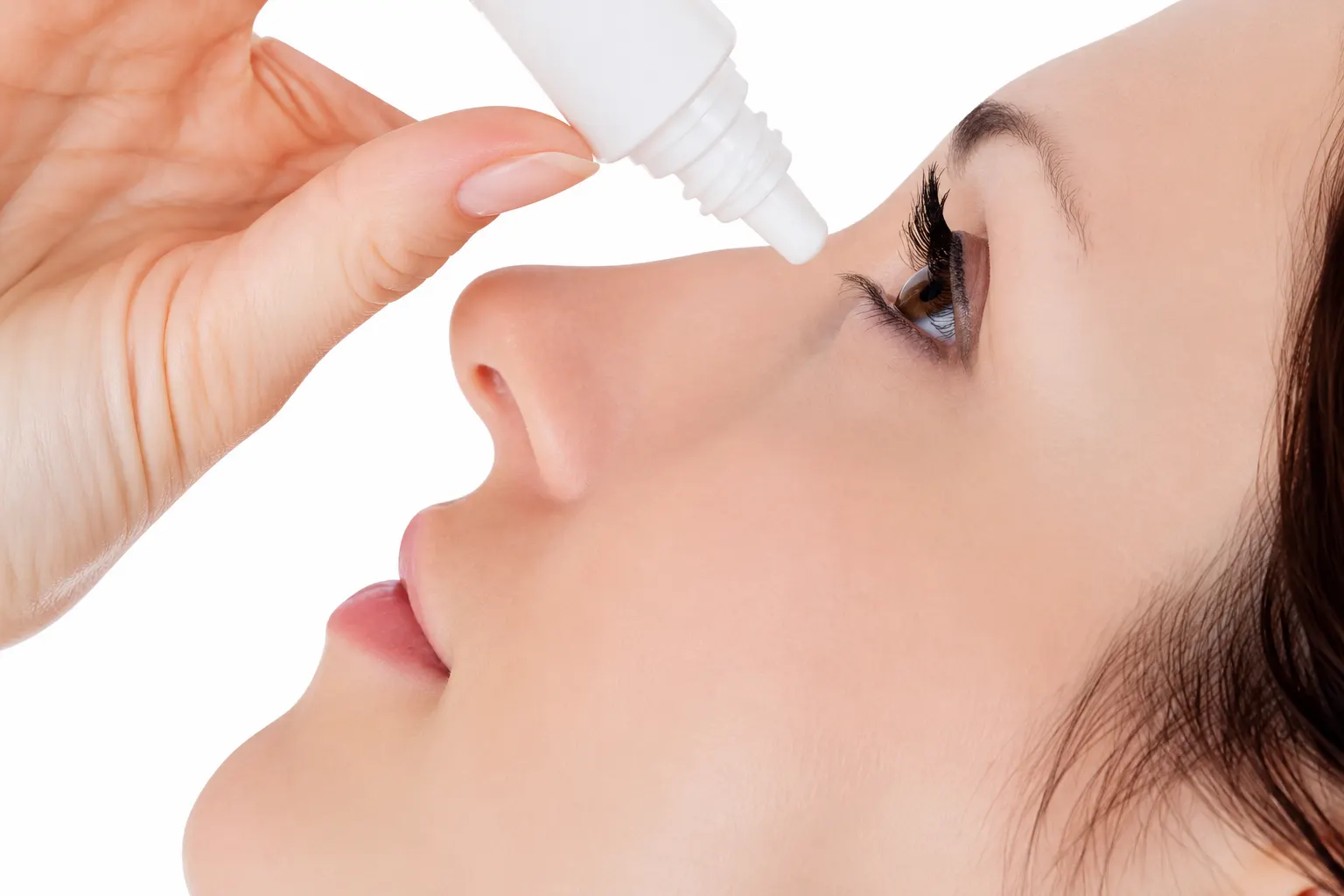 Image of a woman with her head tilted back, aiming a bottle of eye drops into her eye.